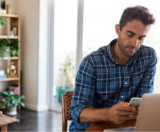 Man looking at phone while sitting at a computer